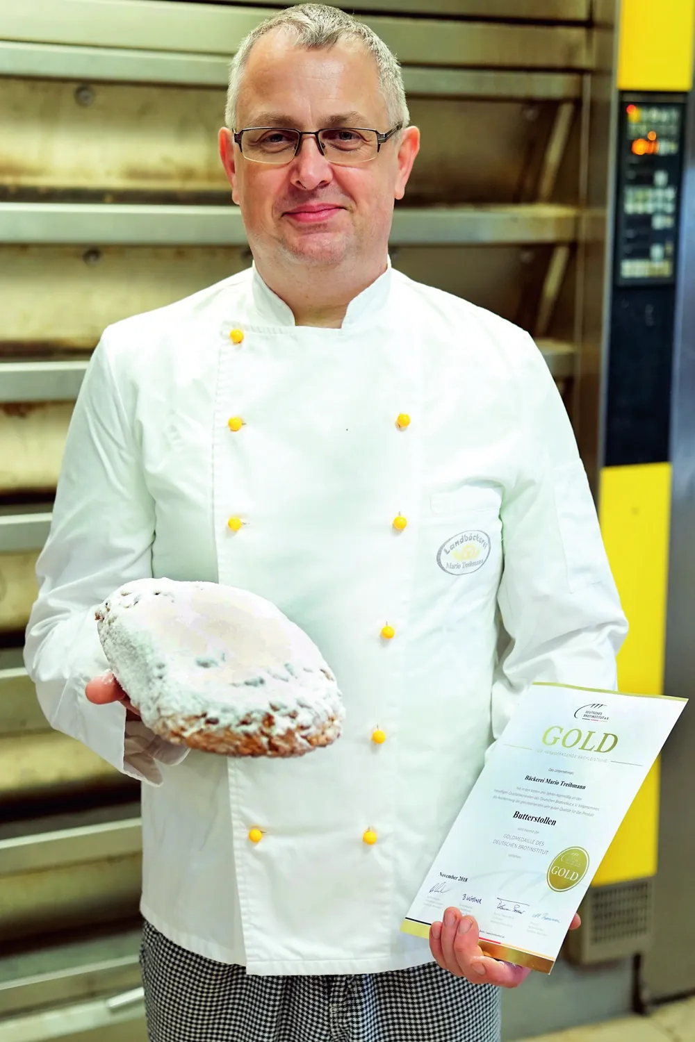Unser Stollenbäcker „Lauser“ in der Backstube vor dem Ofen, mit einem Butterstollen in der einen und der Gold-Urkunde in der anderen Hand